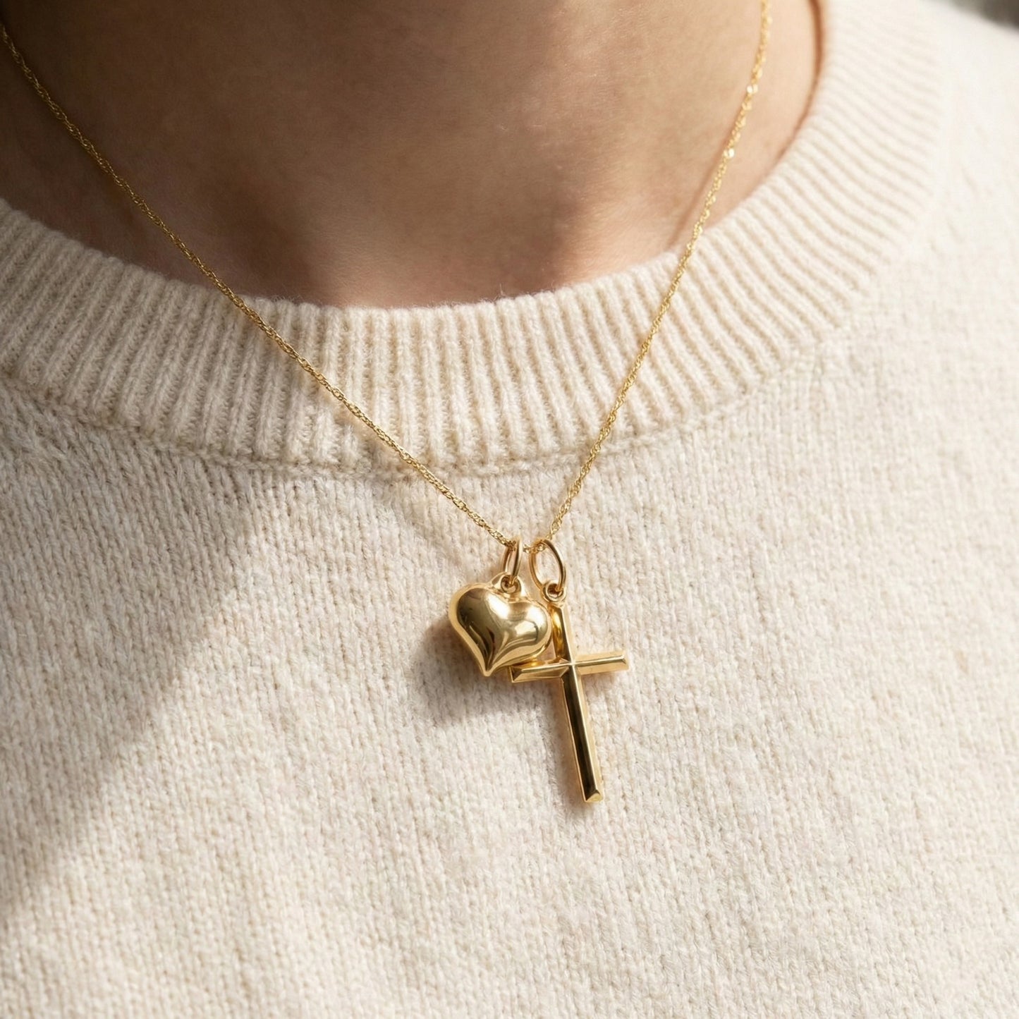 Gold necklace with heart and cross pendants on a light beige sweater.